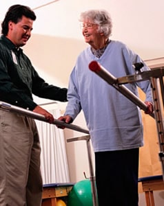 Therapist helping senior woman walk between handrails