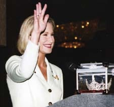 Miss Iowa waving and smiling in front of a crown.