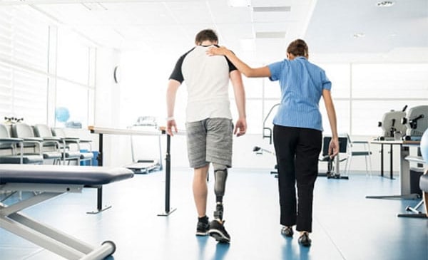 Person with limb loss walking with healthcare worker.